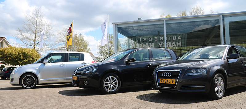 De glazen showroom met de naam Autobedrijf Harry Hagen op de gevel, met occasions op het terrein ervoor