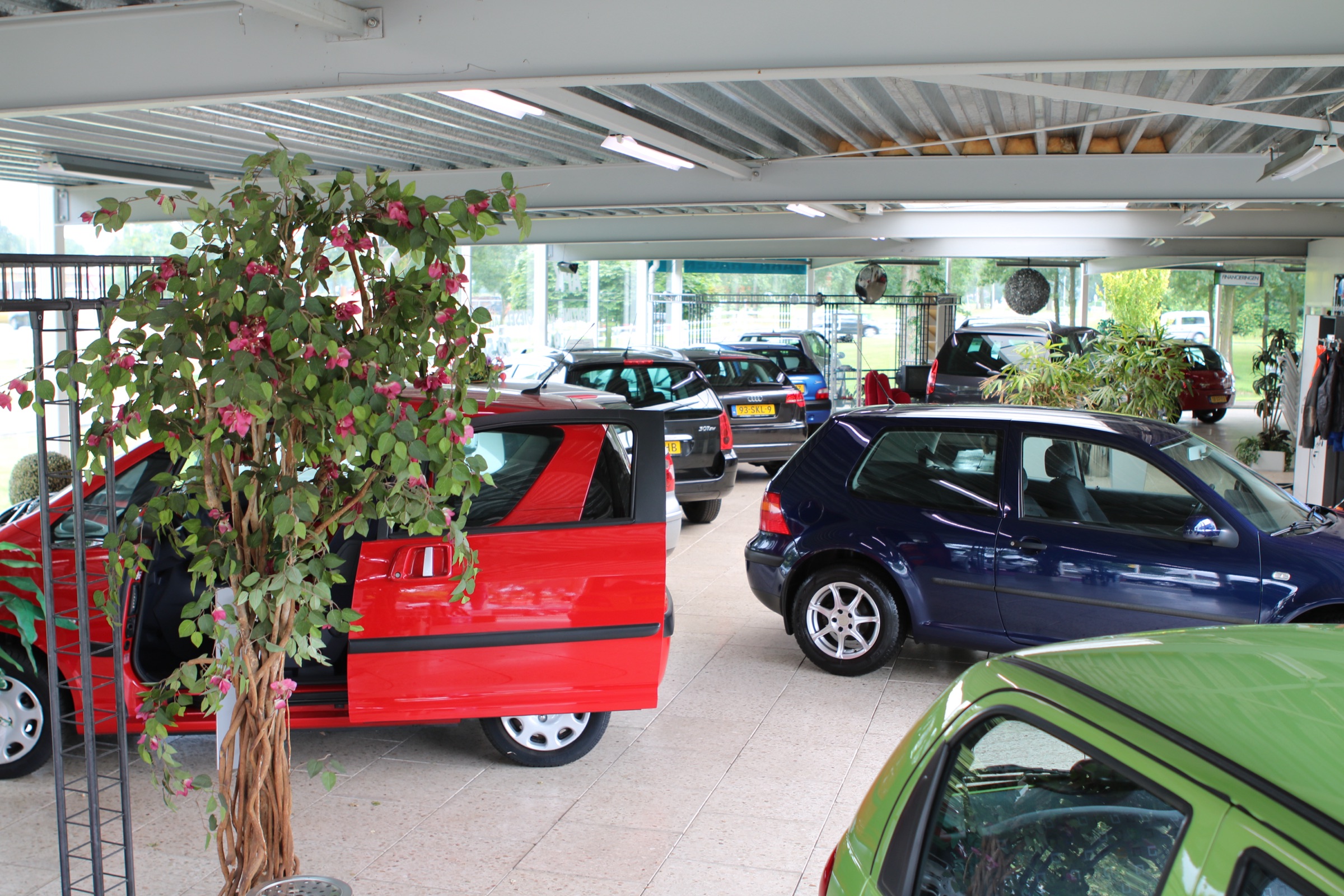 Binnen in de showroom van Autobedrijf Harry Hagen: occasions onder een lichte overkapping