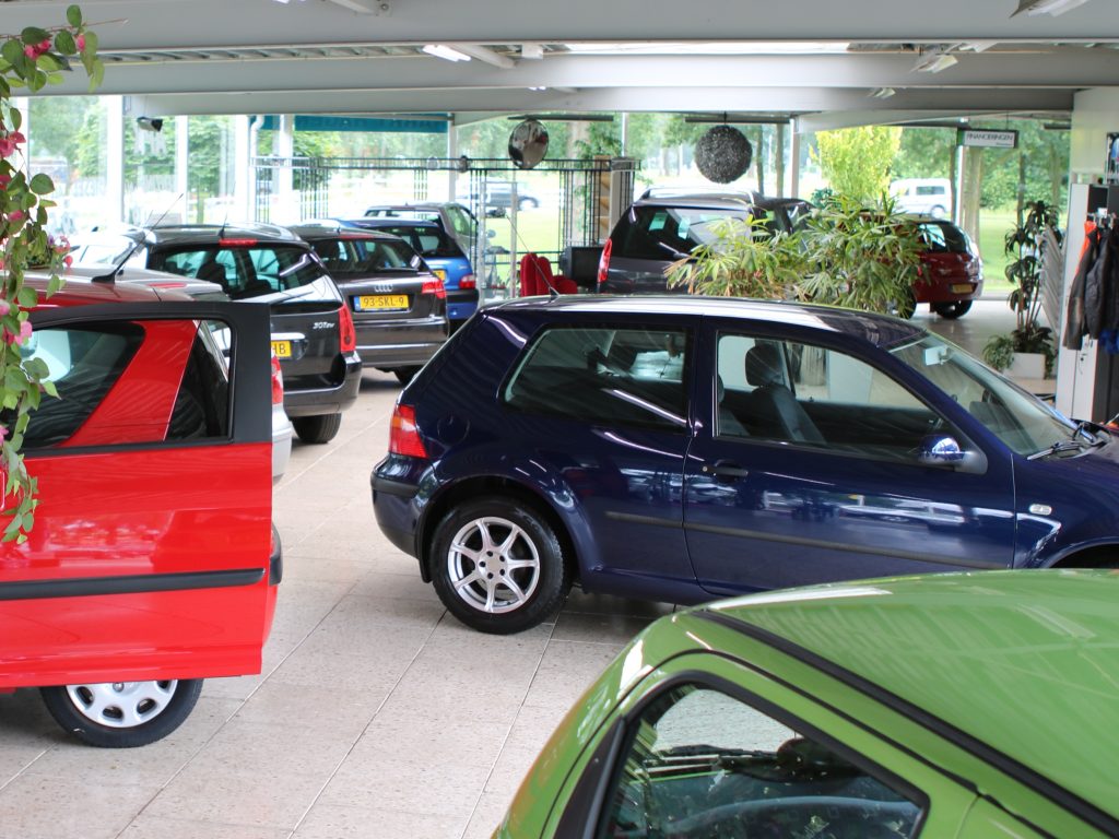 De showroom van Autobedrijf Harry Hagen met een rode Peugeot met open deur, een blauwe Golf en andere occasions onder het dak