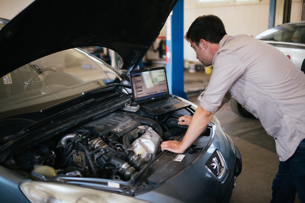 Een monteur doet een diagnose met een laptop bij een auto met open motorkap