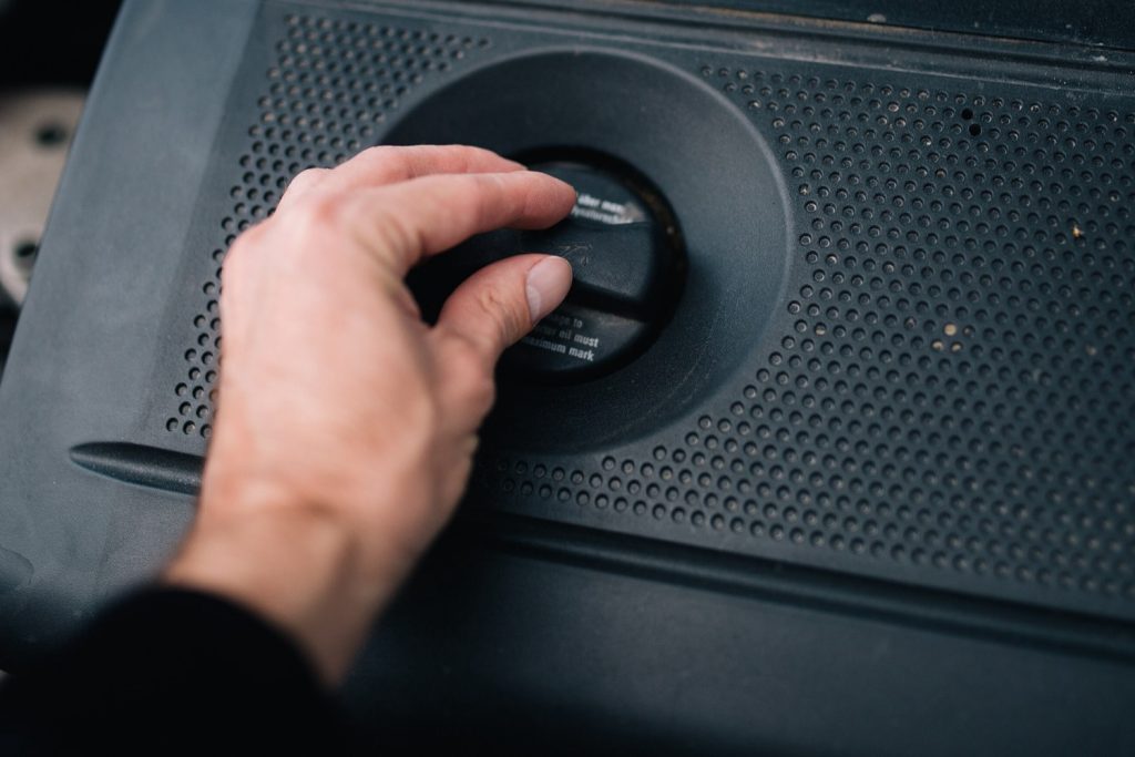 Een hand draait aan de oliedop van een motor
